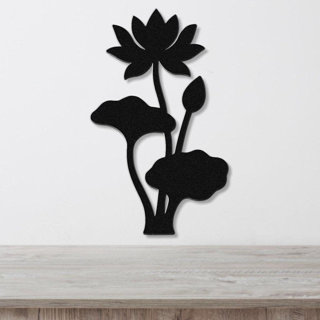 Black metal lotus wall art with a flower, bud, and leaves in a silhouette cutout style, mounted on a white wall above a wooden surface.