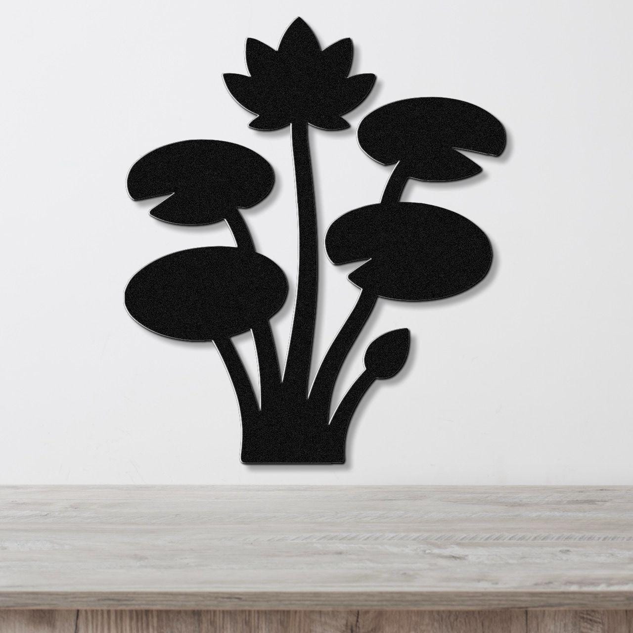 Black metal wall art silhouette of a lotus plant with lily pads and a flower, mounted on a white wall above a wooden surface.
