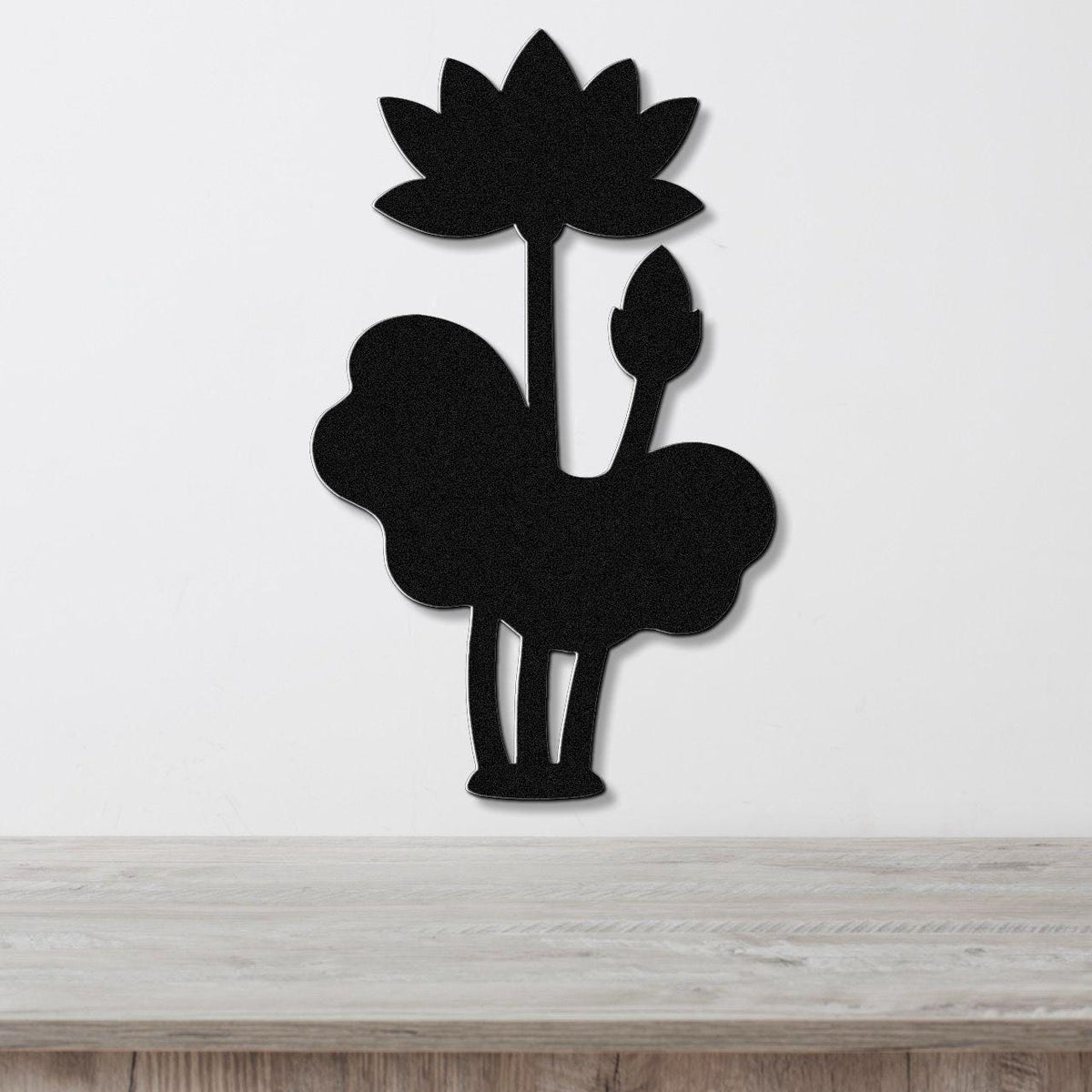 Black metal wall art silhouette of a lotus flower and leaves, mounted on a white wall above a wooden surface.