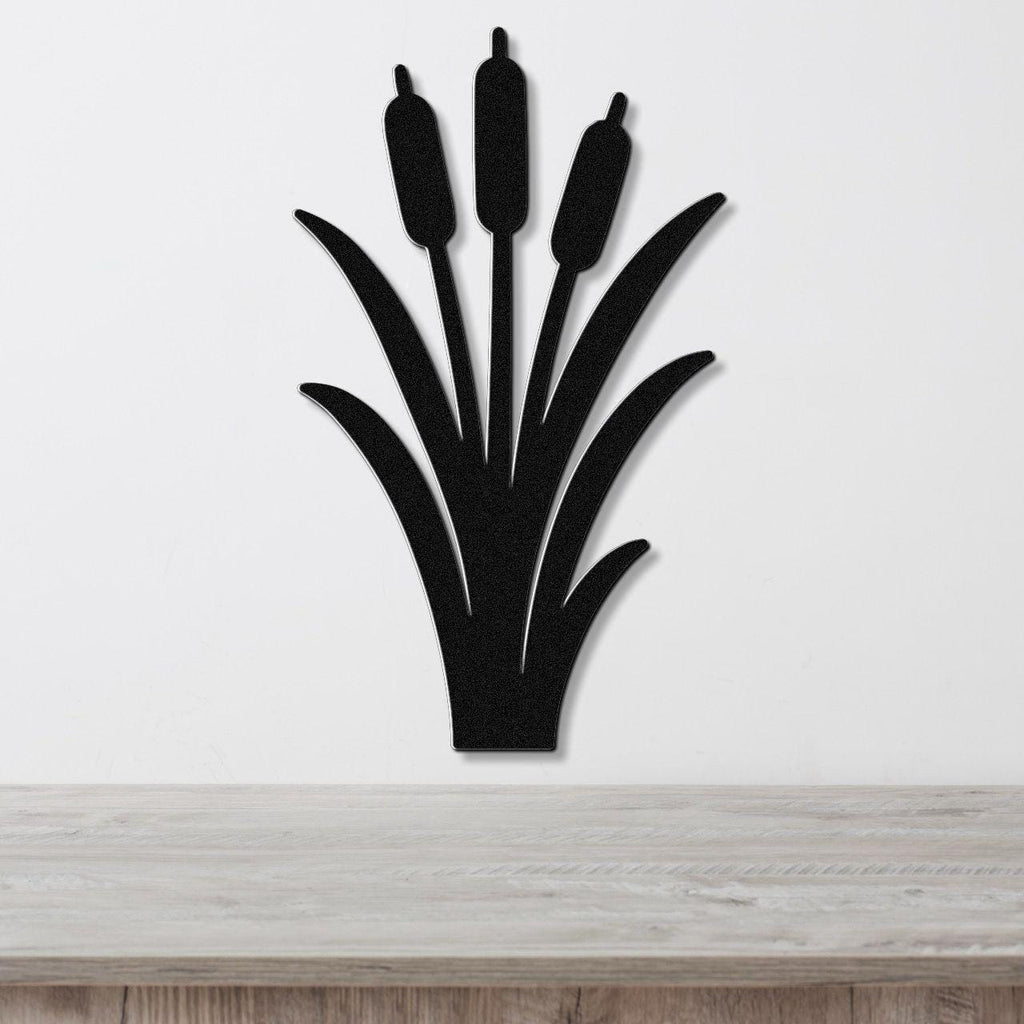 Black metal wall art silhouette of cattails with three seed heads and long leaves, mounted on a white wall above a light wood surface.