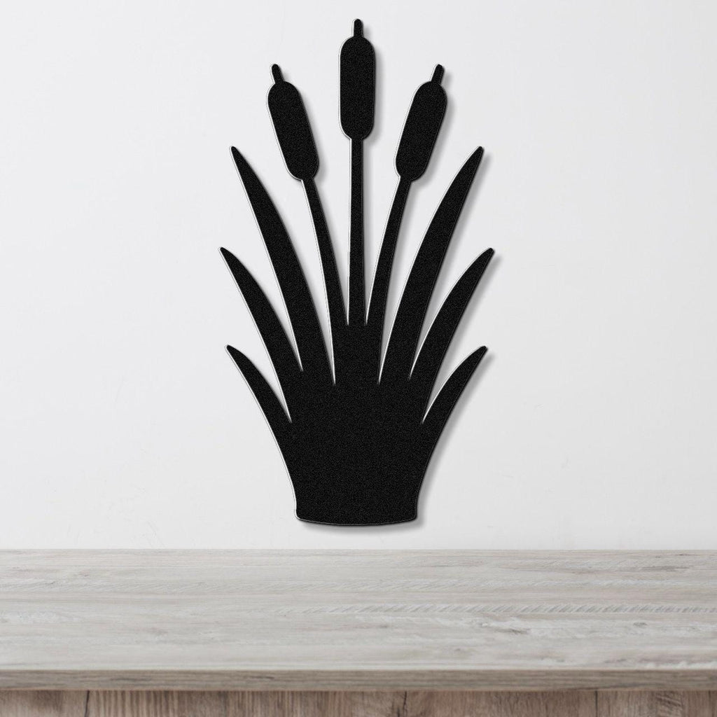 Black metal cattail wall art with a silhouette design of three seed heads and long leaves, mounted on a white wall above a light wood surface.