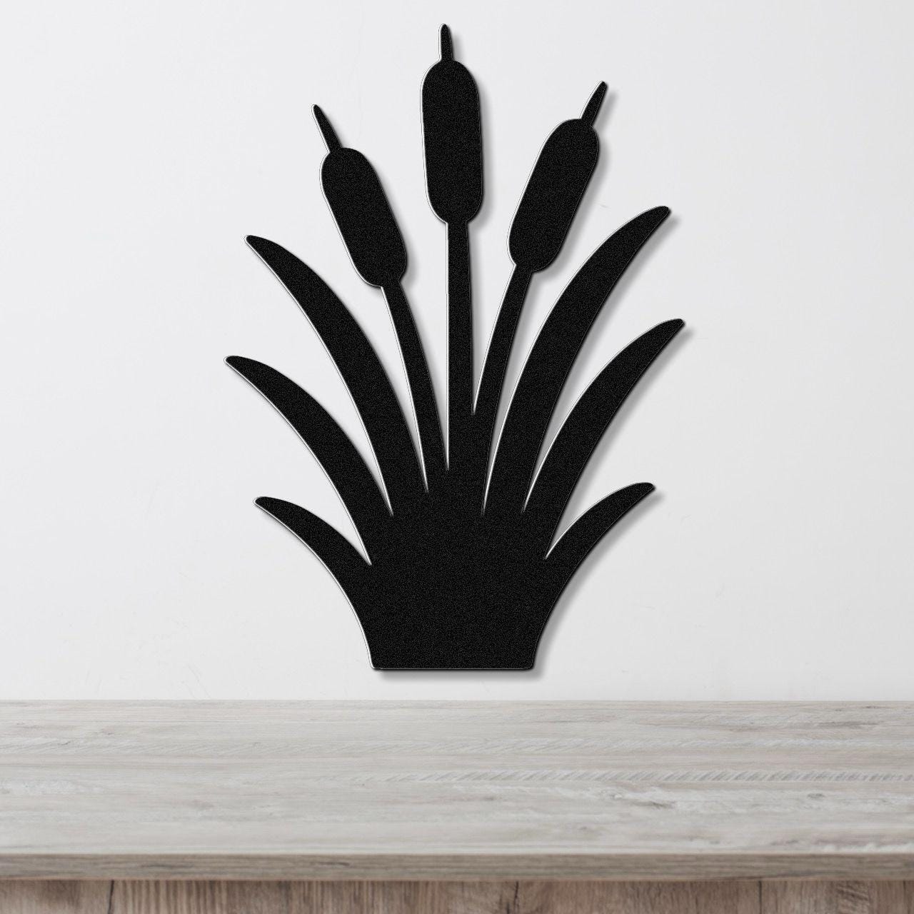 Black metal cattail wall art silhouette with three seed heads and long leaves, mounted on a white wall above a light wood surface.