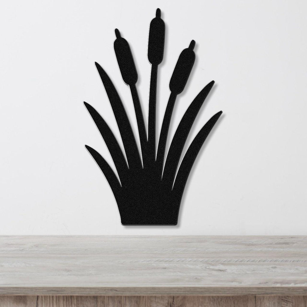 Black metal cattail wall art with a silhouette design of three seed heads and long leaves, mounted on a white wall above a light wood surface.