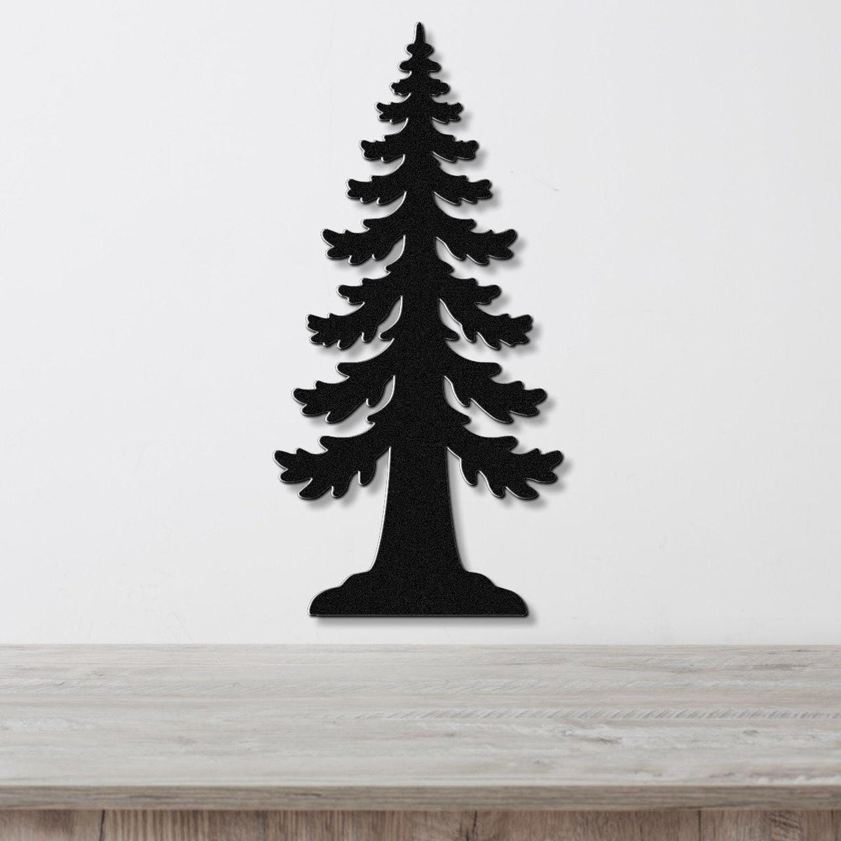 Black metal wall art in the silhouette of a sequoia tree with layered branch cutouts, mounted on a white wall above a light wood surface.