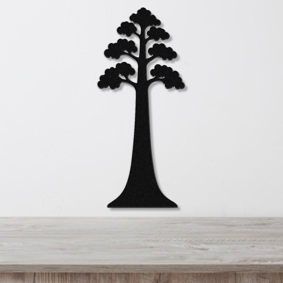 Black metal wall art in the silhouette of a sequoia tree with layered canopy cutouts, mounted on a white wall above a light wood surface.