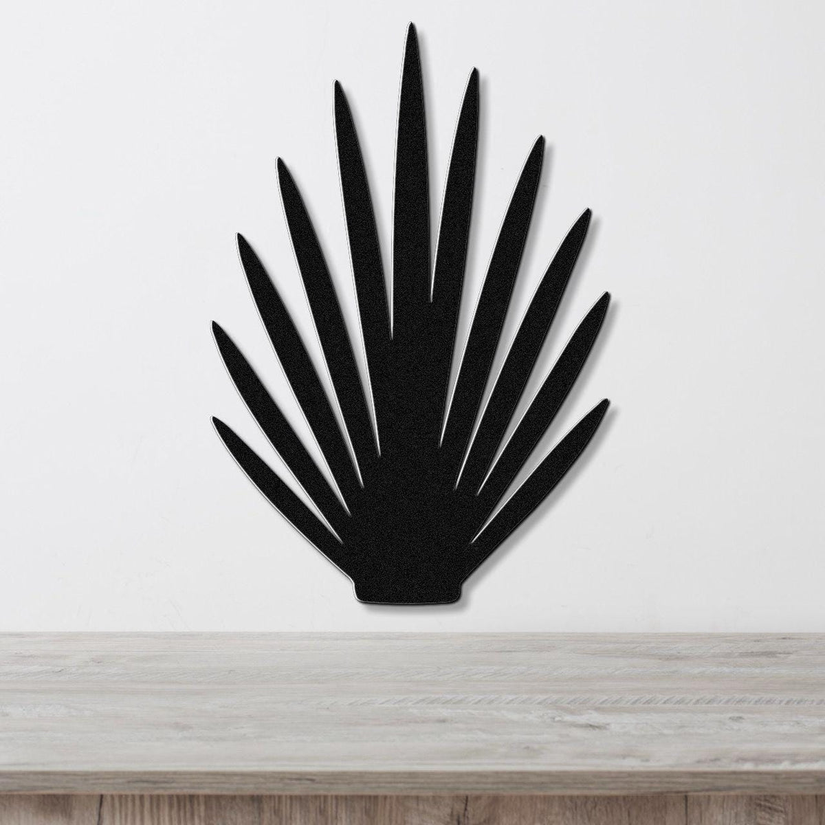 Black metal wall art in a fan-shaped silhouette with pointed rays, mounted on a white wall above a light wood surface.