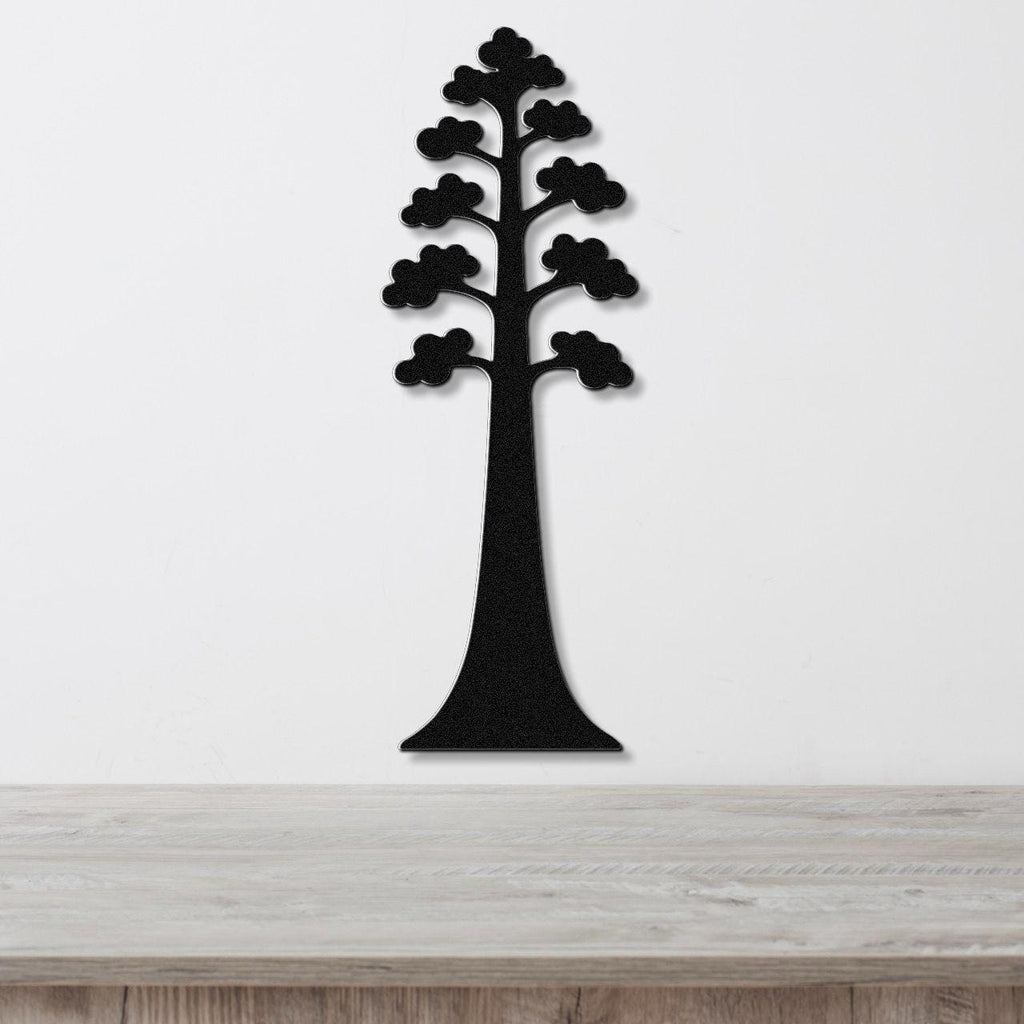 Black metal wall art in the silhouette of a sequoia tree with layered branches, mounted on a white wall above a wooden surface.