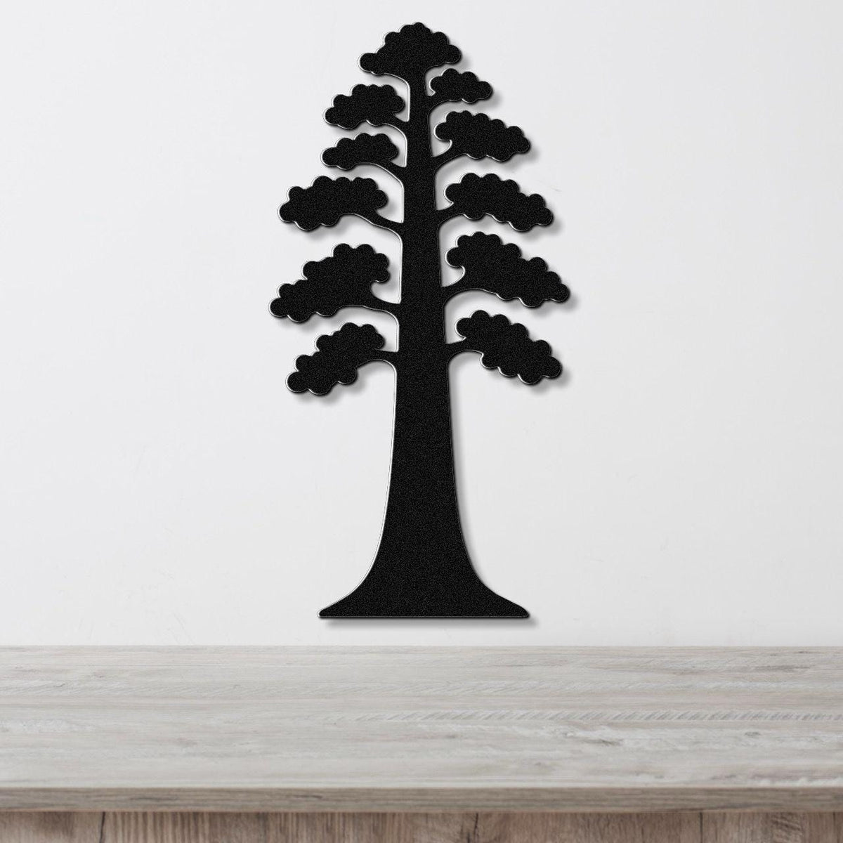 Black metal wall art in the silhouette of a sequoia tree with layered branch cutouts, mounted on a white wall above a light wood surface.