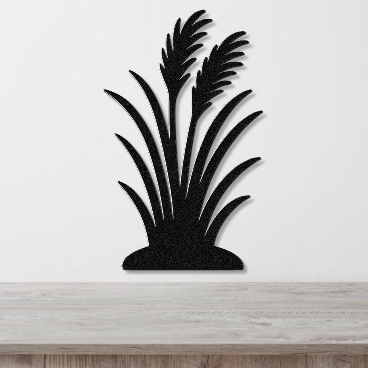 Black metal wall art in a wild grass silhouette design, mounted on a white wall above a light wood countertop.