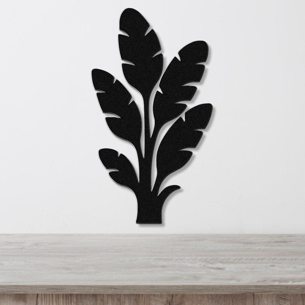 Black metal wall art in a tropical leaf silhouette design with layered cutouts, mounted on a white wall above a light wood surface.