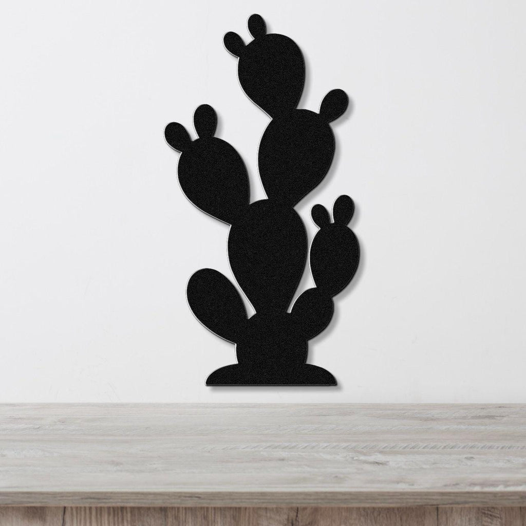 Black metal cactus wall art with layered paddle shapes, mounted on a white wall above a light wood surface.