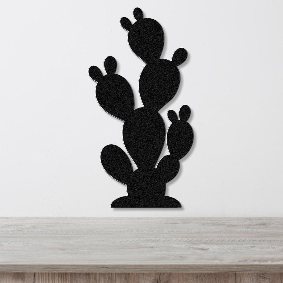 Black metal cactus wall art with layered paddle shapes, mounted on a white wall above a light wood surface.