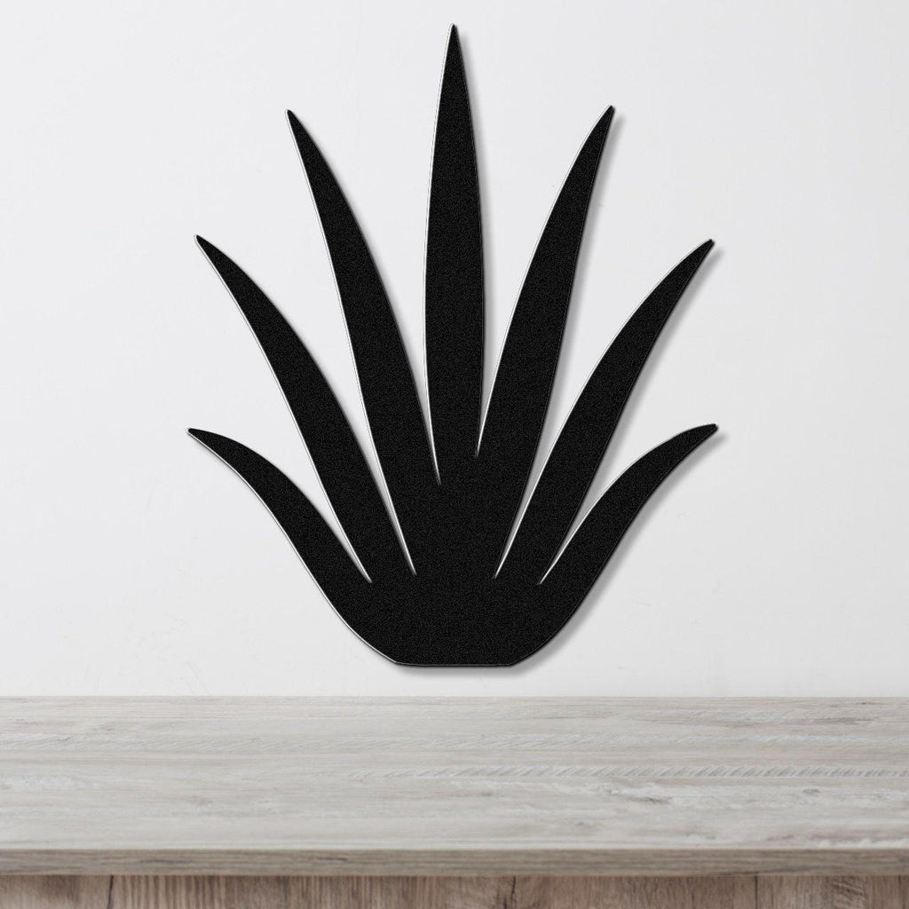 Black metal wall art cutout of a century plant with spiky leaves, mounted on a white wall above a light wood surface.