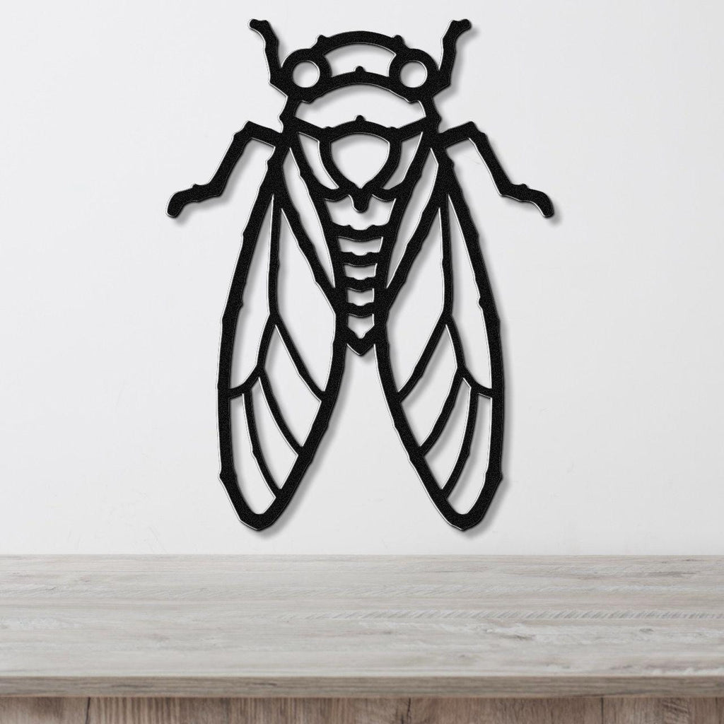 Black metal cicada wall art with detailed wing and body cutouts, mounted on a white wall above a light wood countertop.