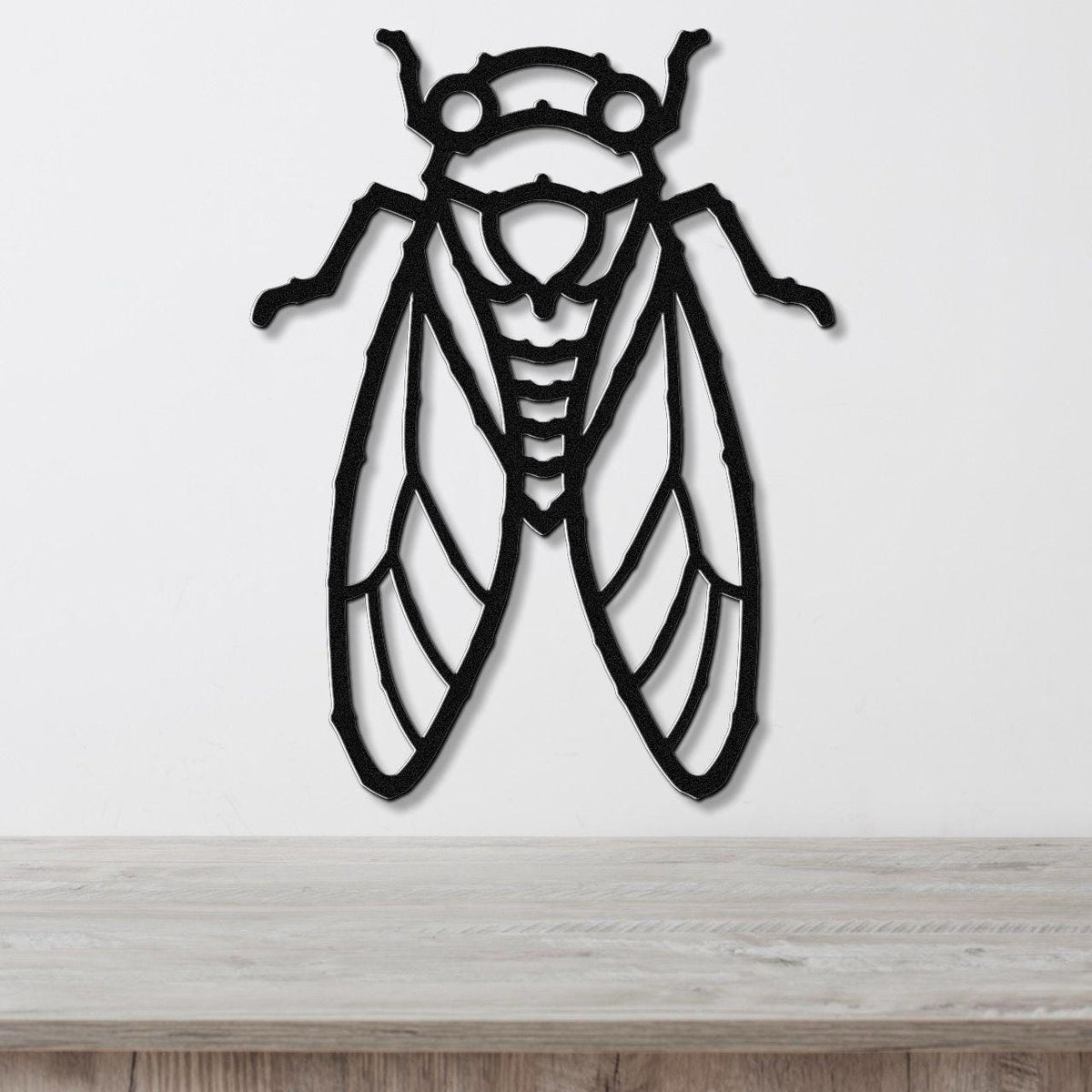Black metal cicada wall art with detailed wing and body cutouts, mounted on a white wall above a light wood countertop.