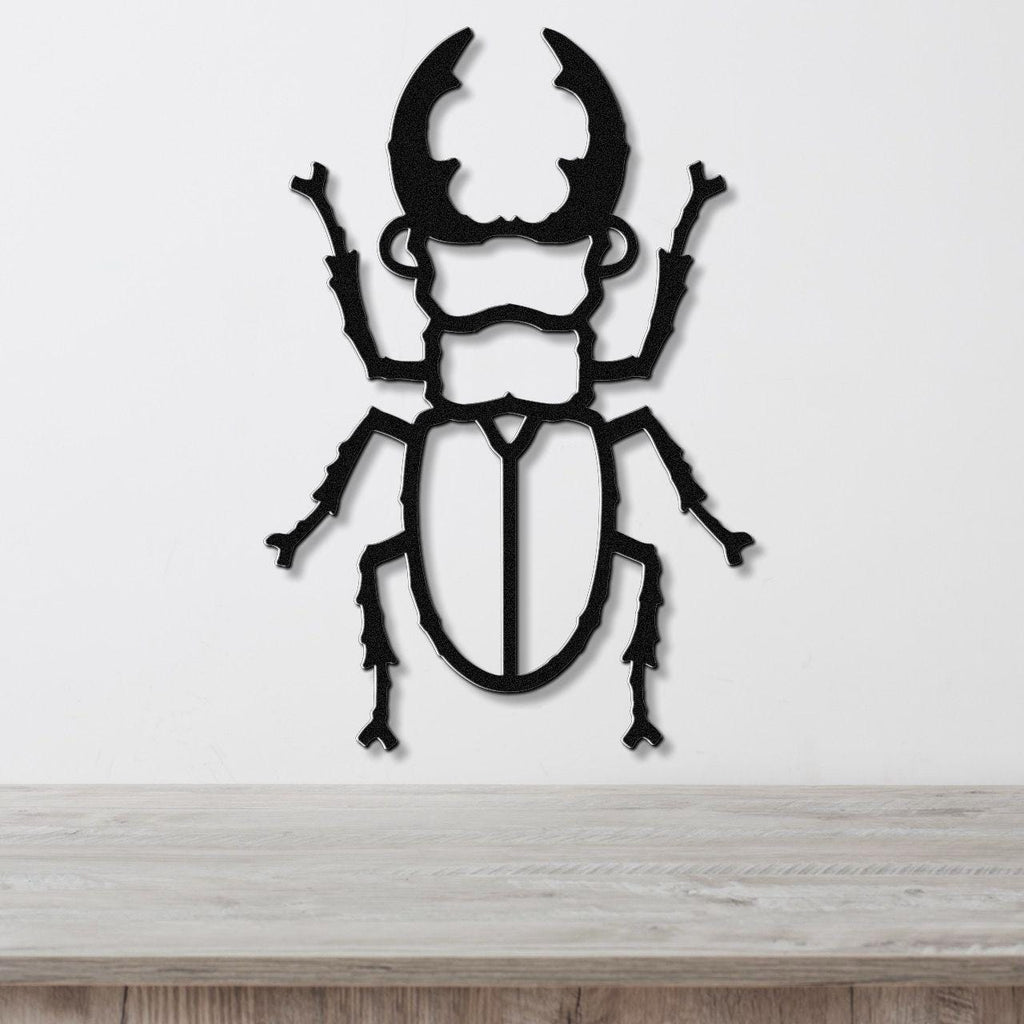 Black metal wall art in the silhouette of a beetle with large curved horns and detailed legs, mounted on a white wall above a wooden surface.