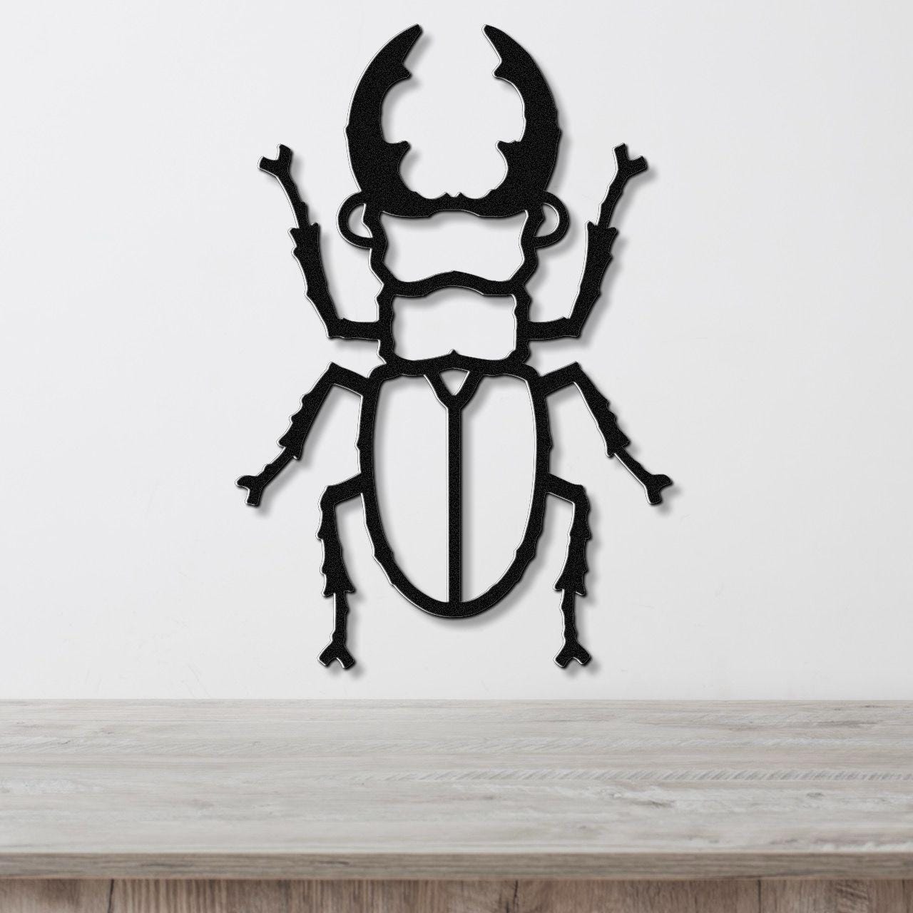 Black metal wall art in the silhouette of a beetle with large curved horns and detailed legs, mounted on a white wall above a wooden surface.