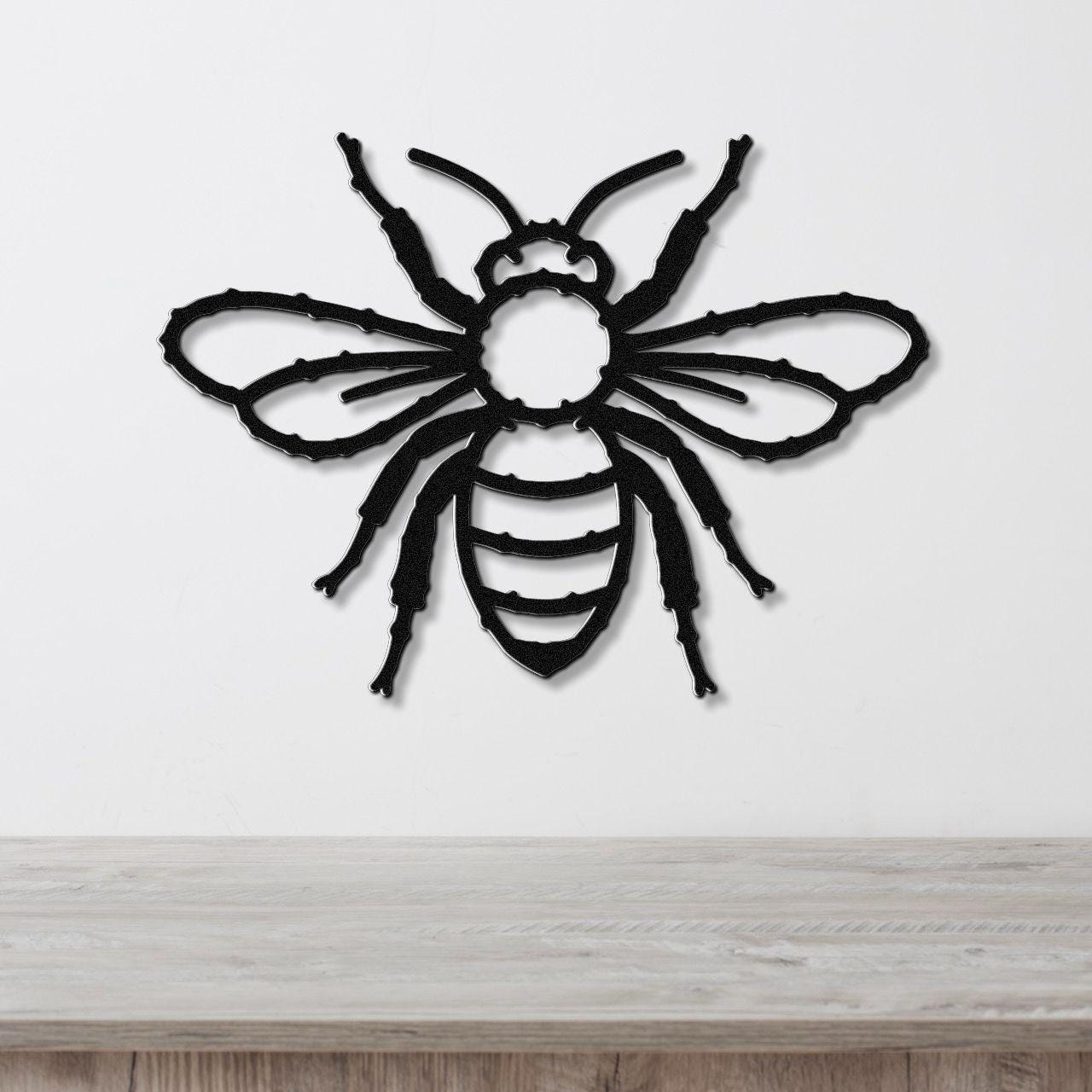 Black metal bee wall art with cutout wings and striped body, mounted on a white wall above a light wood surface.