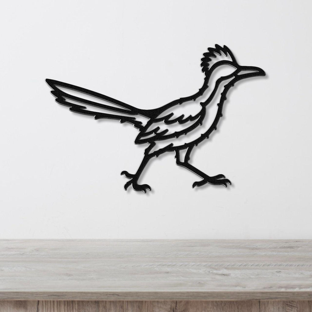Black metal roadrunner wall art with detailed feather and tail cutouts, mounted on a white wall above a light wood surface.