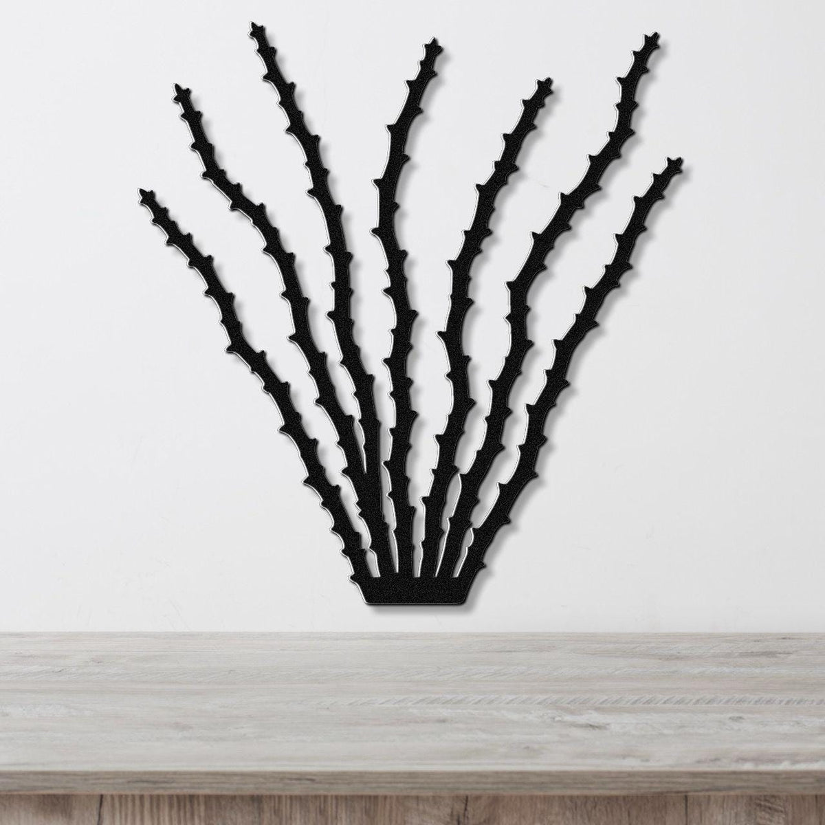Black metal ocotillo wall art with spiky branch cutouts, mounted on a white wall above a light wood counter.