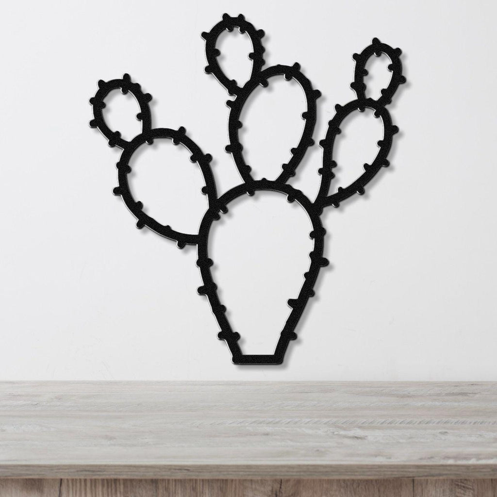 Black metal wall art cutout of a prickly pear cactus with spiny edges, mounted on a white wall above a light wood surface.