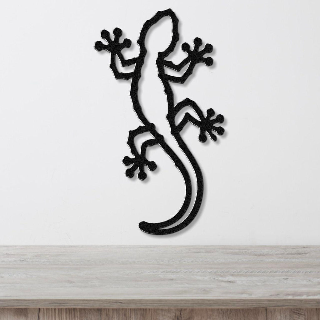 Black metal gecko wall art with detailed cutout limbs and tail, mounted on a white wall above a light wood countertop.