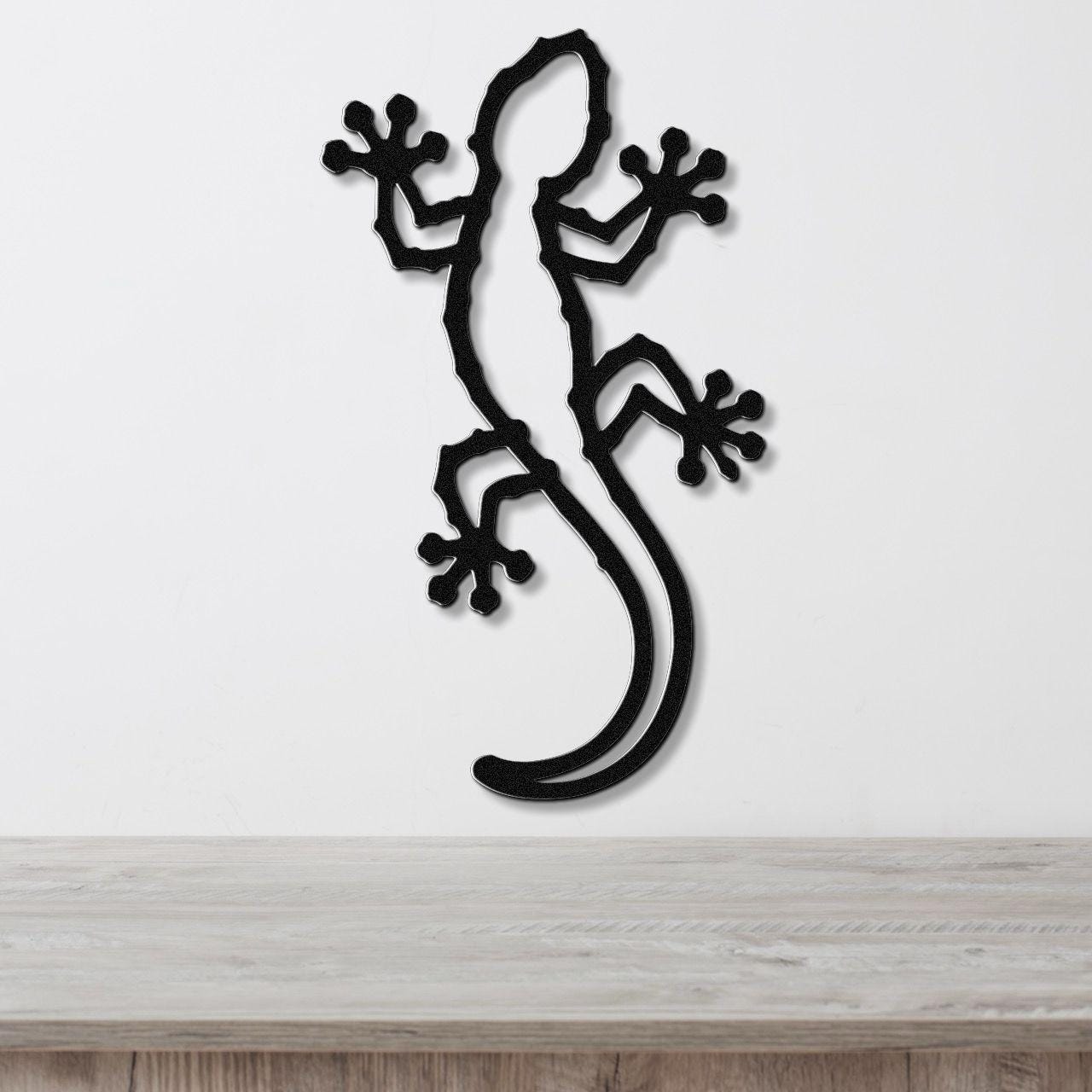 Black metal gecko wall art with detailed cutout limbs and tail, mounted on a white wall above a light wood countertop.