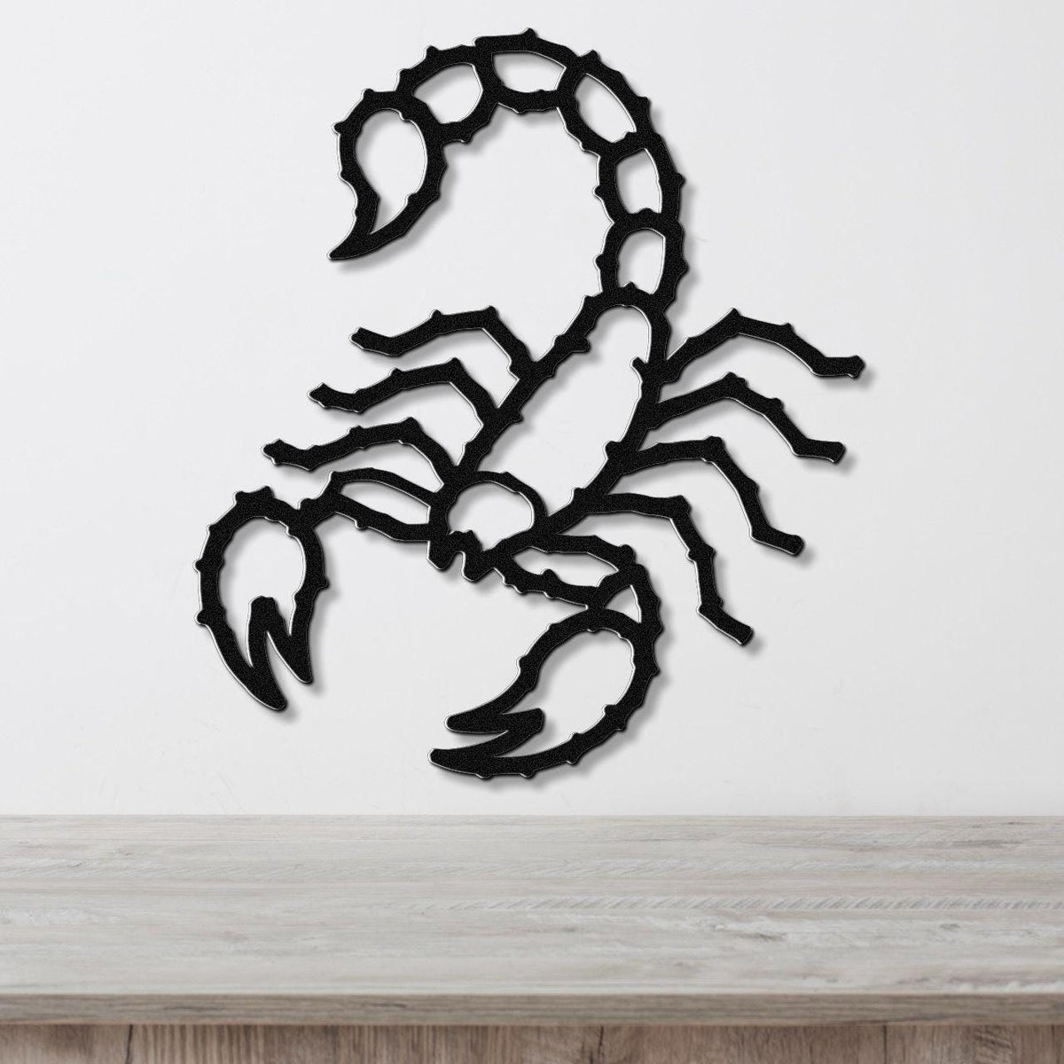 Black metal scorpion wall art with detailed cutout segments, mounted on a white wall above a light wood surface.