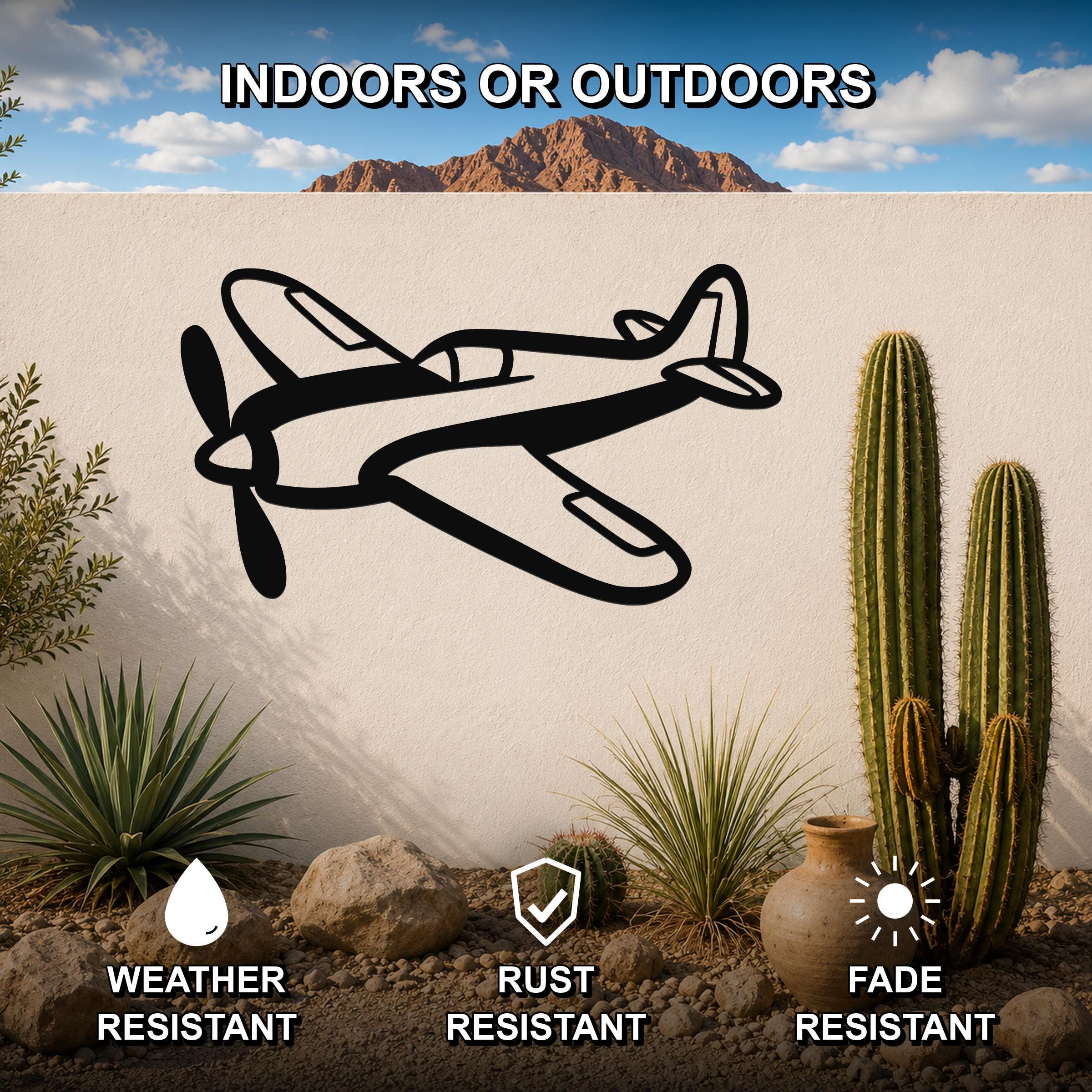 Black metal airplane wall art with a bold silhouette design, mounted on an outdoor wall in a desert garden setting with cacti and rocks.
