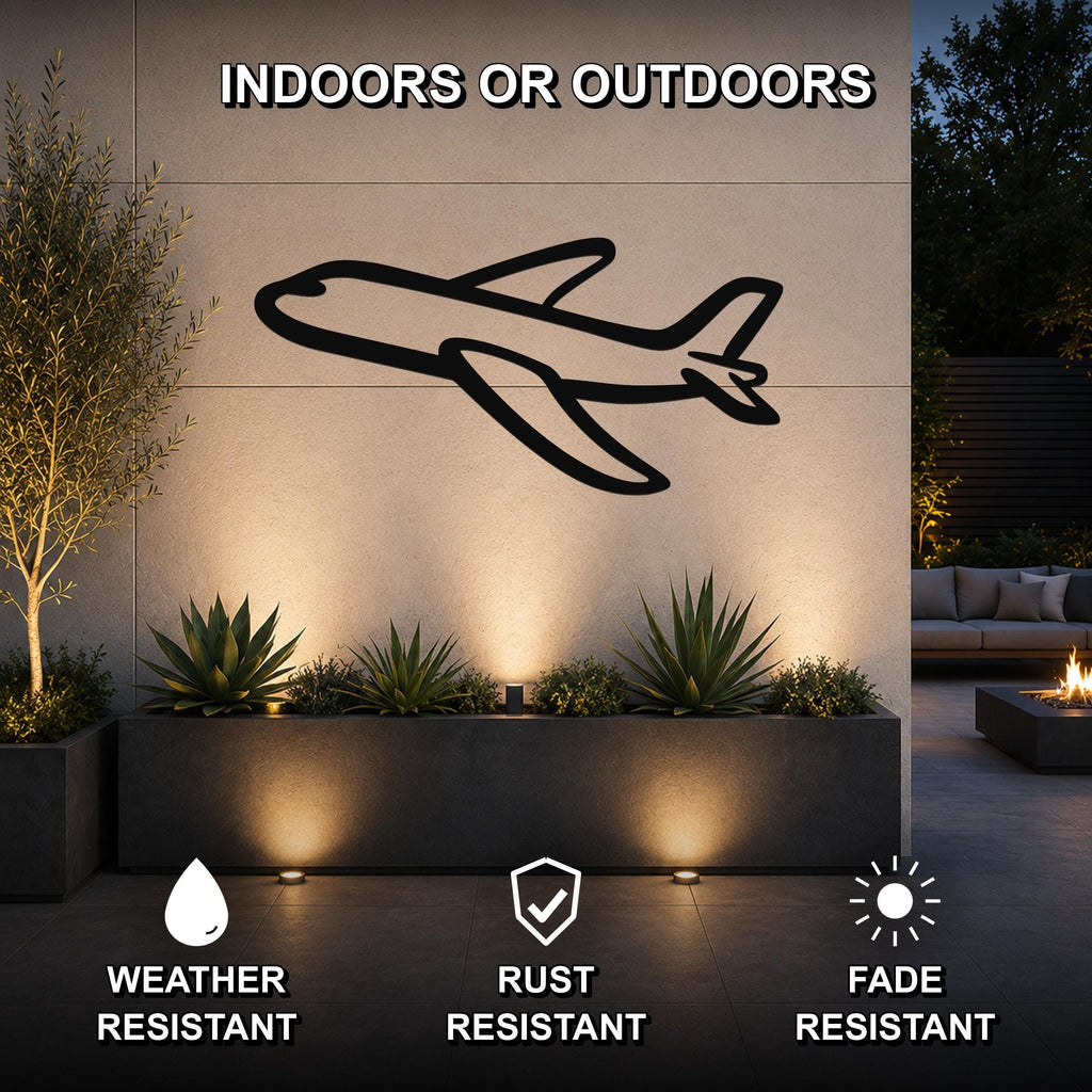 Black metal airplane wall art silhouette mounted on an outdoor wall above a planter, illuminated by ground lights in a patio setting.