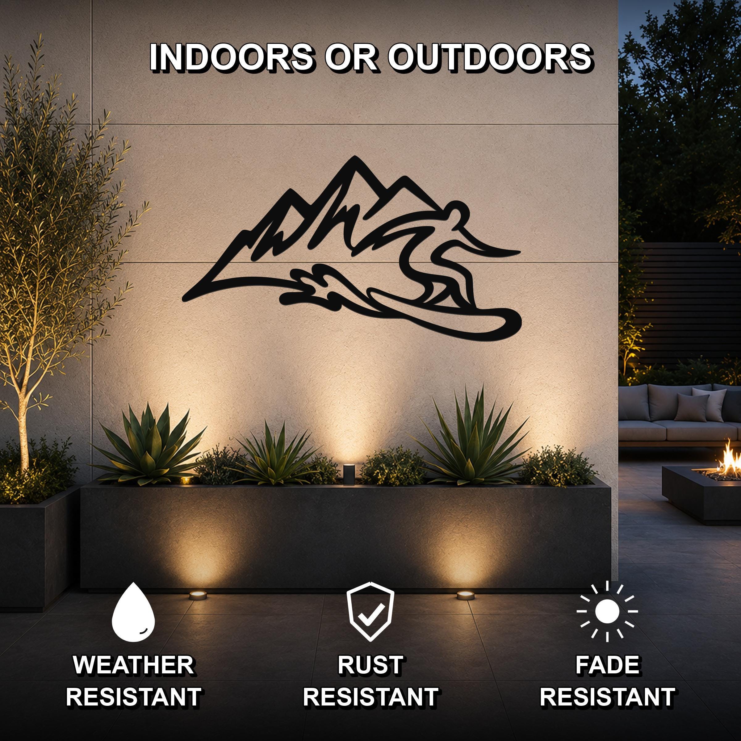 Black metal wall sculpture of a snowboarder in motion above a planter, mounted on an outdoor wall in a modern patio setting.