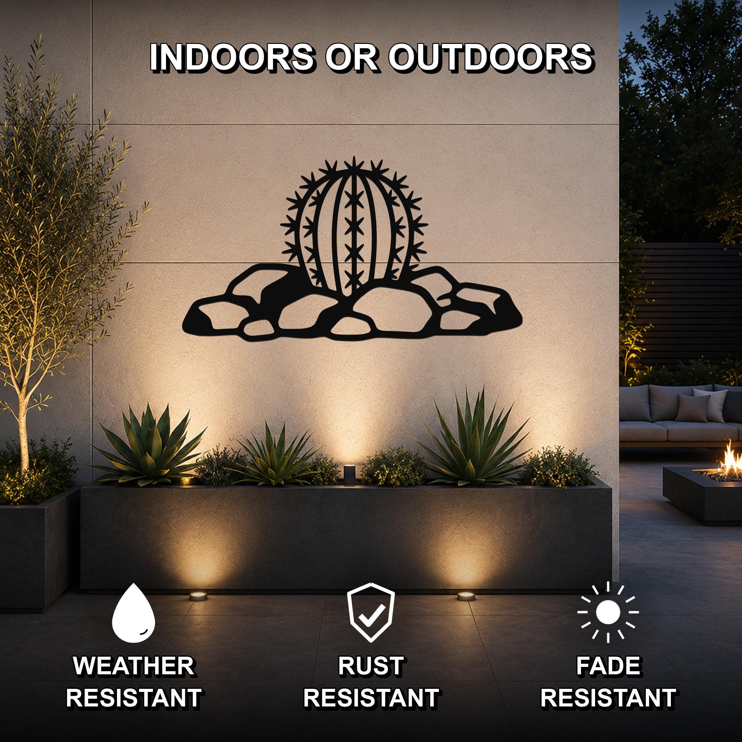 Black metal barrel cactus wall art with spines and rocks cutout, mounted on an outdoor wall above a planter in a patio setting.