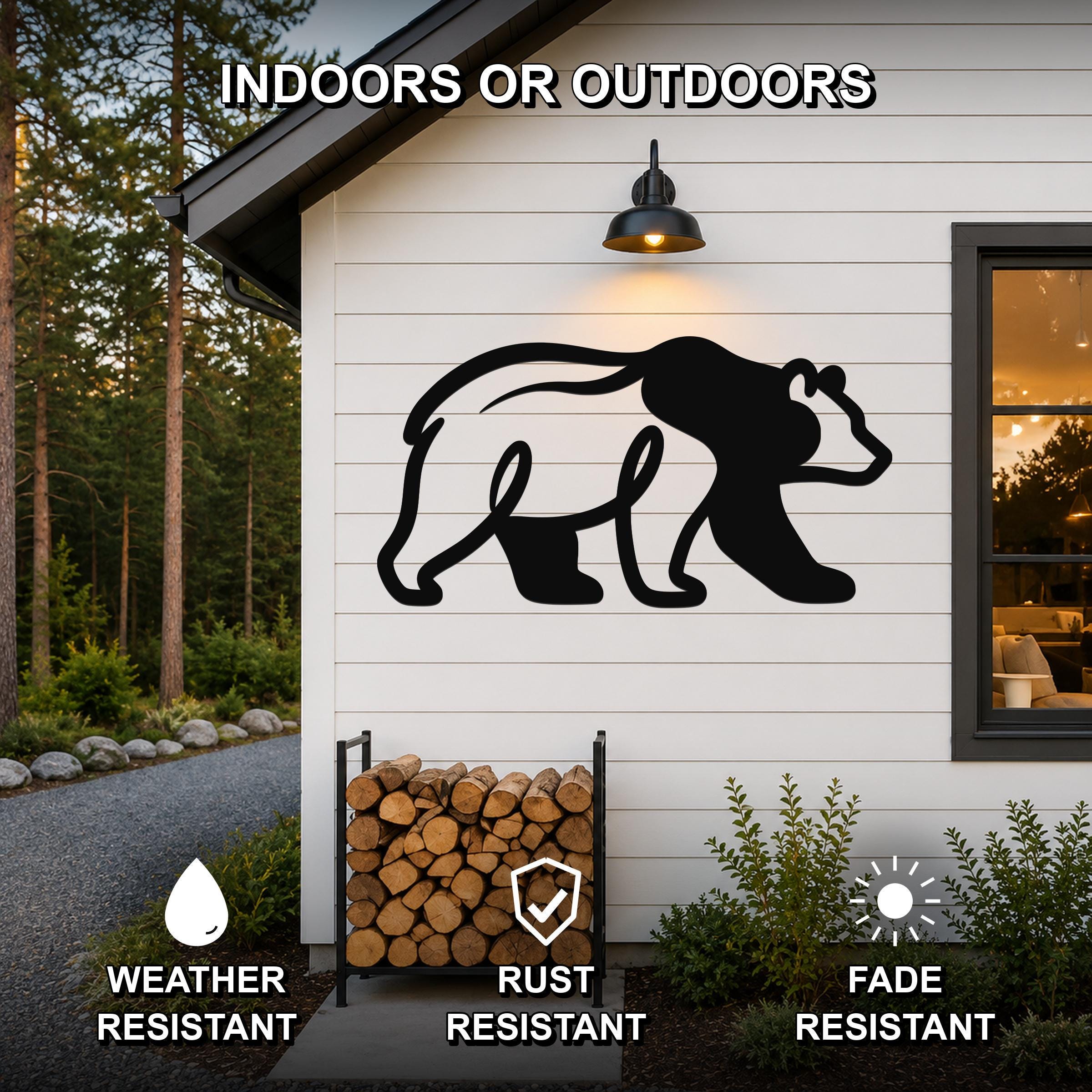 Black metal bear silhouette wall art mounted on a white siding exterior wall above a firewood rack, with text indicating it is weather, rust, and fade resistant for indoor or outdoor use.