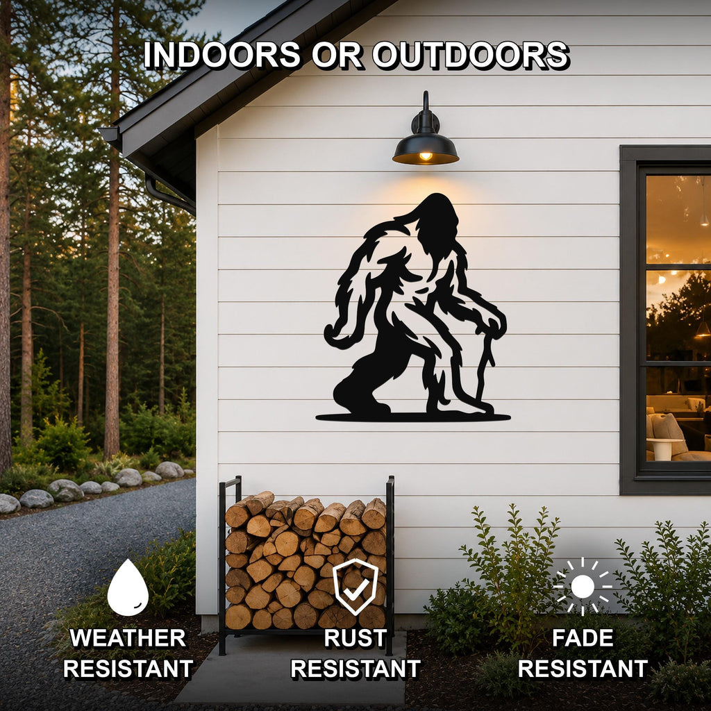 Black metal Bigfoot silhouette wall art mounted on a white siding exterior wall above a firewood rack, with text indicating it is weather, rust, and fade resistant for indoor or outdoor use.