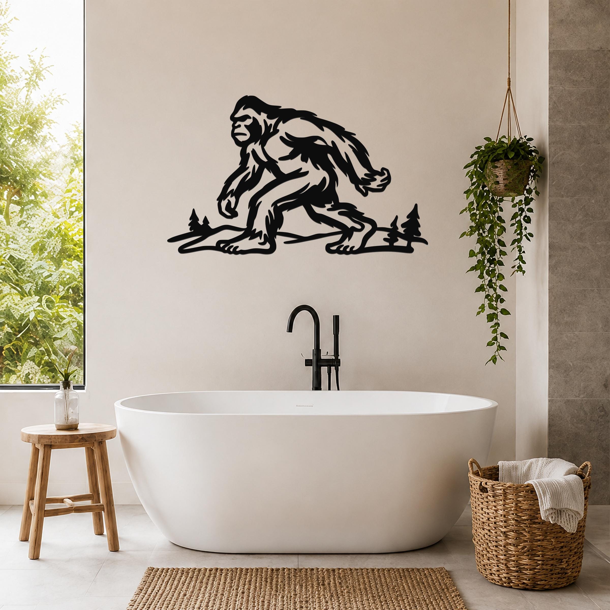 Black metal Bigfoot wall art silhouette with tree cutouts, mounted above a freestanding bathtub in a modern bathroom.
