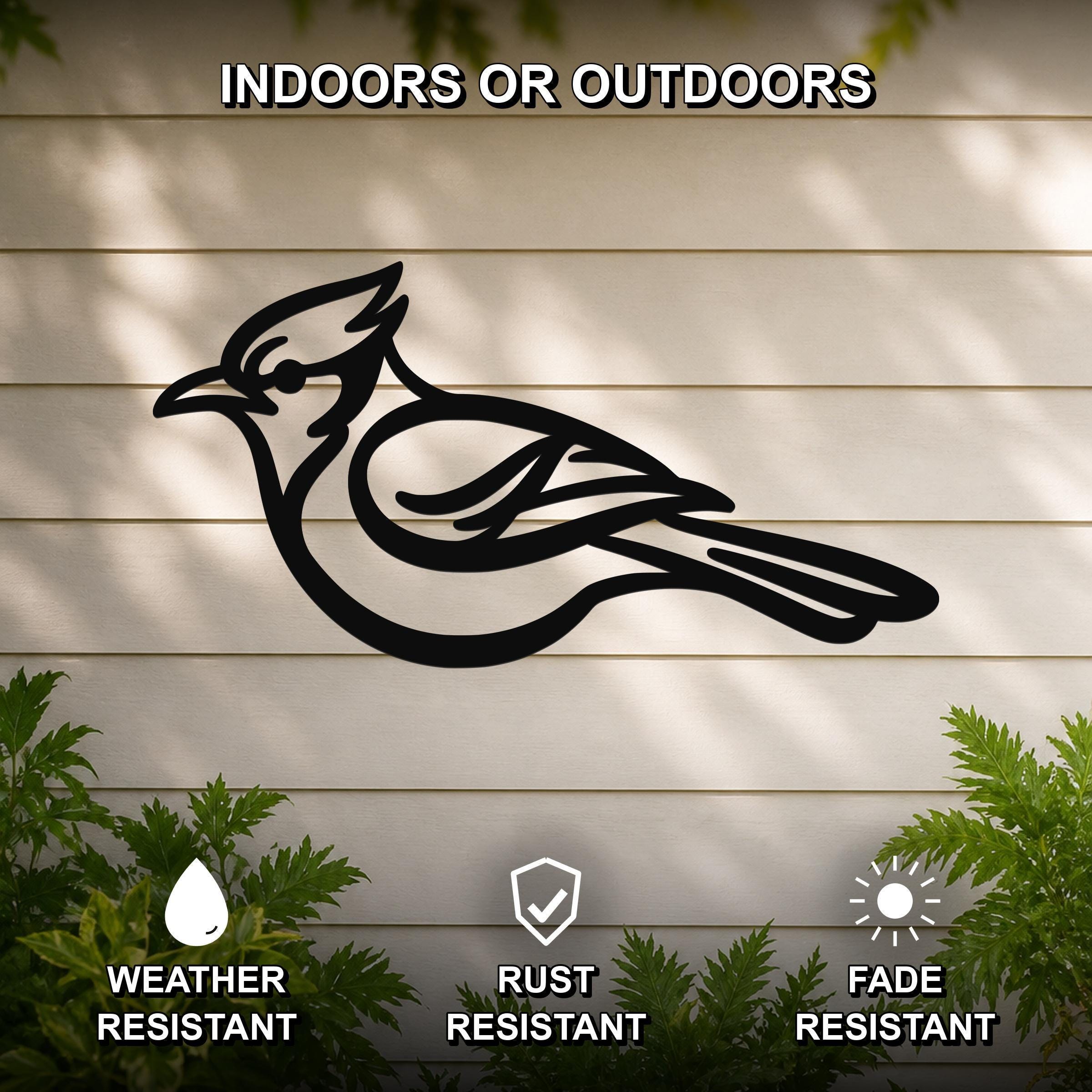 Black metal blue jay wall art silhouette mounted on a beige outdoor wall, with green plants at the base and text indicating it is weather, rust, and fade resistant.