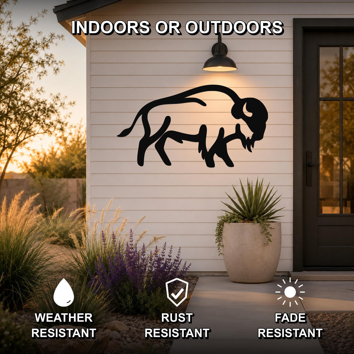 Black metal buffalo silhouette wall art mounted on a white siding exterior wall above a patio, with a potted plant and garden in the foreground.