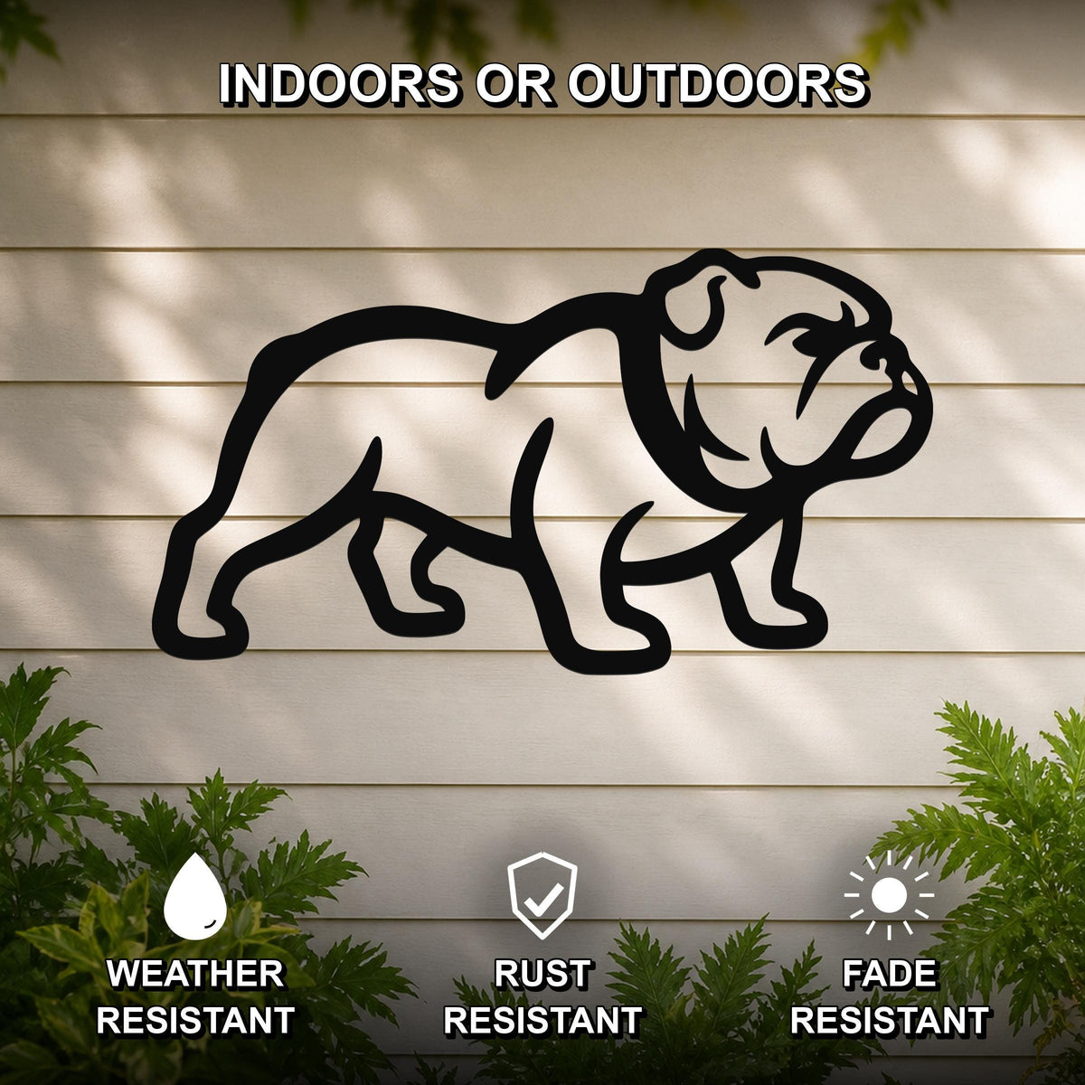 Black metal bulldog wall art silhouette mounted on a light-colored outdoor wall, with green plants at the base and text indicating it is weather, rust, and fade resistant.