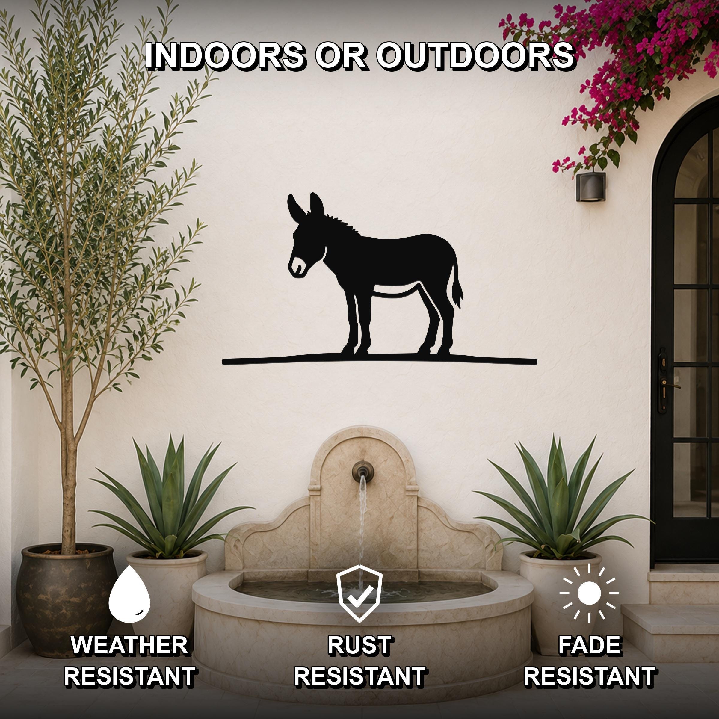 Black metal donkey wall art silhouette mounted on an outdoor wall above a stone fountain, flanked by potted plants and a flowering vine.