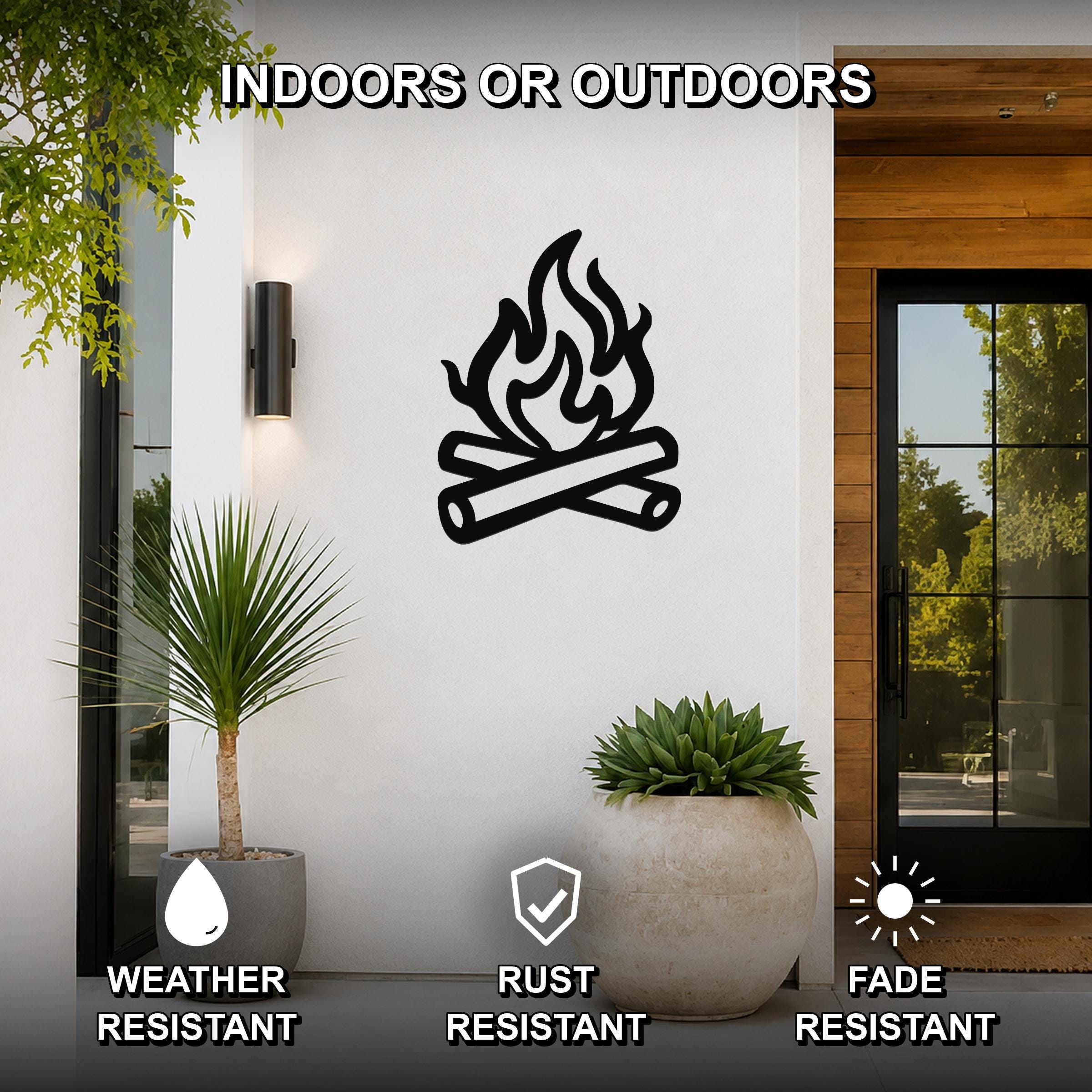 Black metal campfire wall art with crossed logs and flame silhouette, mounted on a white exterior wall beside a glass door and potted plants.