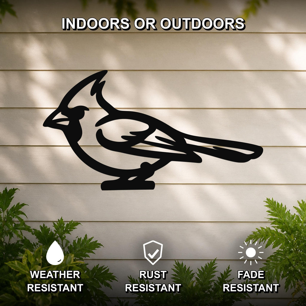 Black metal cardinal wall art in silhouette form, mounted on a light-colored outdoor wall with greenery below, weather resistant, rust resistant, and fade resistant.