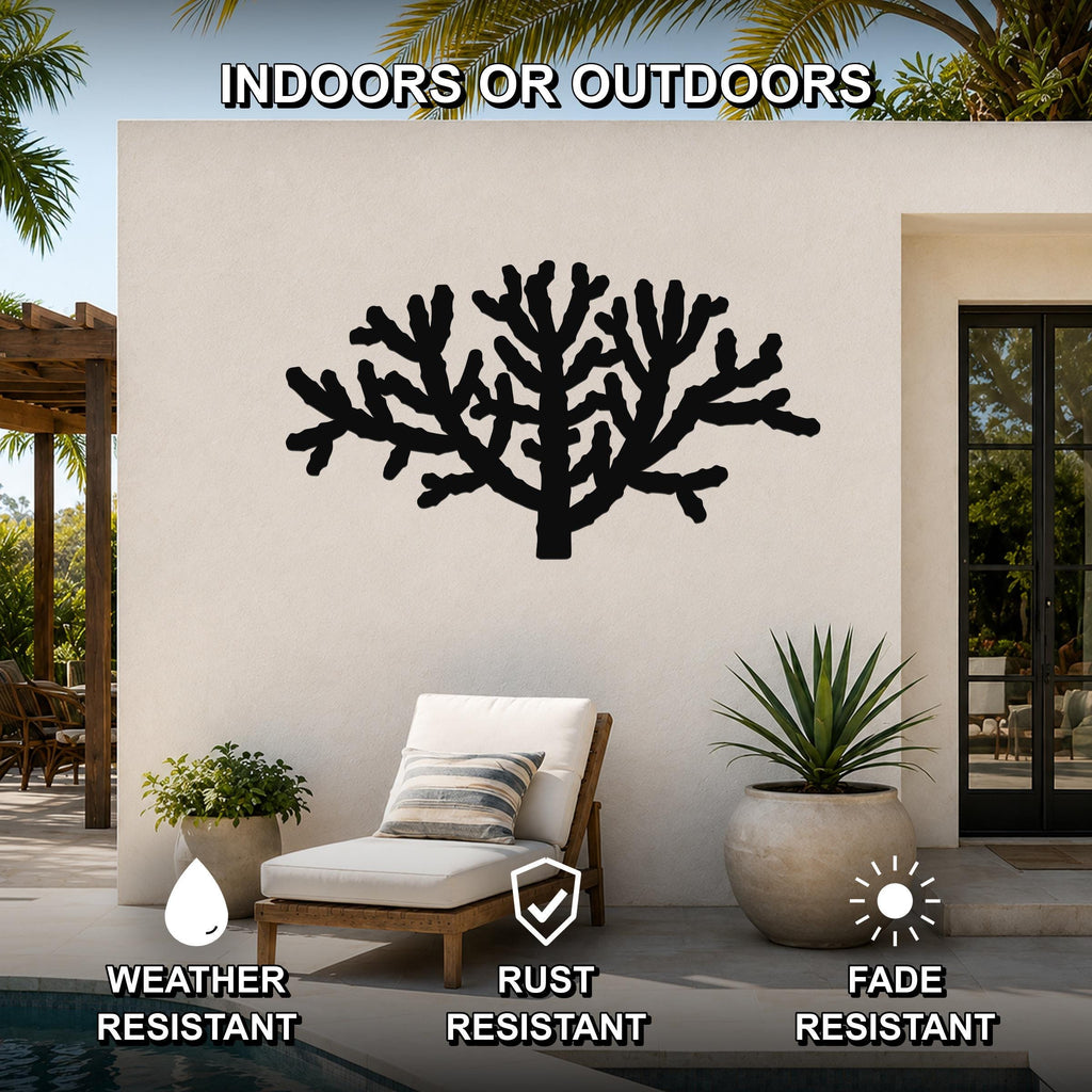 Black metal Cholla cactus wall art silhouette mounted on an outdoor patio wall, featuring intricate branching cutouts and positioned above a lounge chair near a pool.