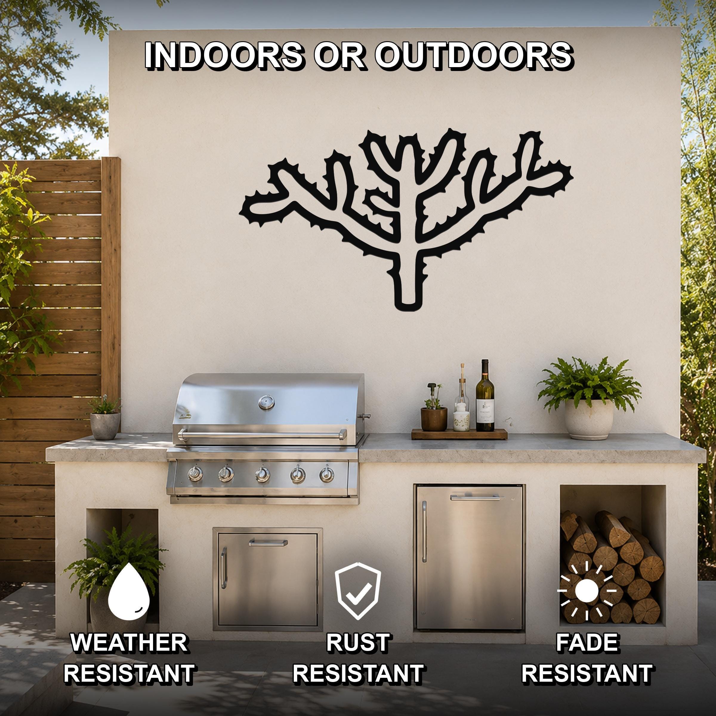Black metal Cholla cactus wall art with spiky branch cutouts, mounted on an outdoor kitchen wall above a stainless steel grill.