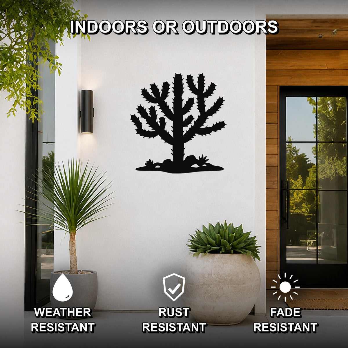 Black metal Cholla cactus wall art silhouette with spiny branches and base cutouts, mounted on a white exterior wall beside a glass door and potted plants.