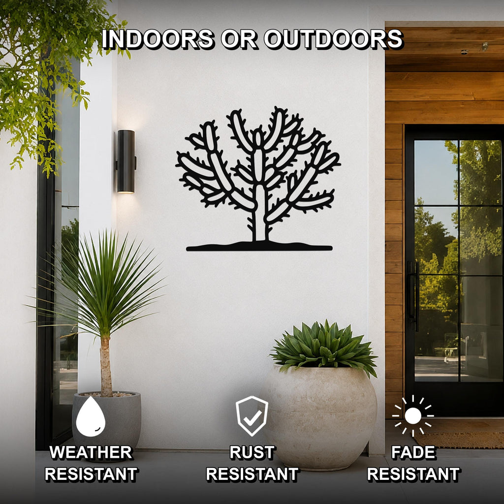 Black metal cholla cactus wall art with branching cutouts, mounted on a white exterior wall beside a glass door and potted plants.