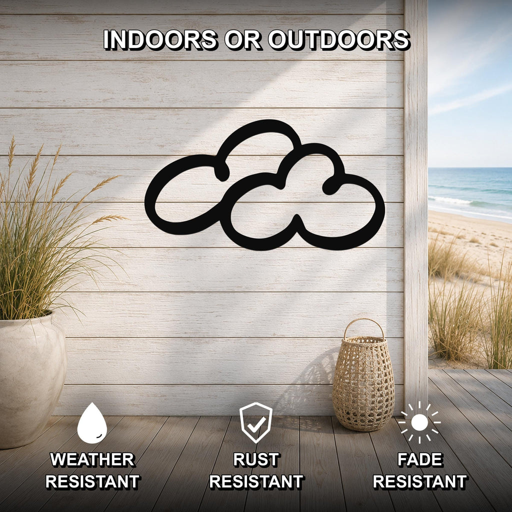 Black metal cloud wall art with a cutout silhouette, mounted on a light wood plank wall in a coastal indoor-outdoor space with a view of the beach.