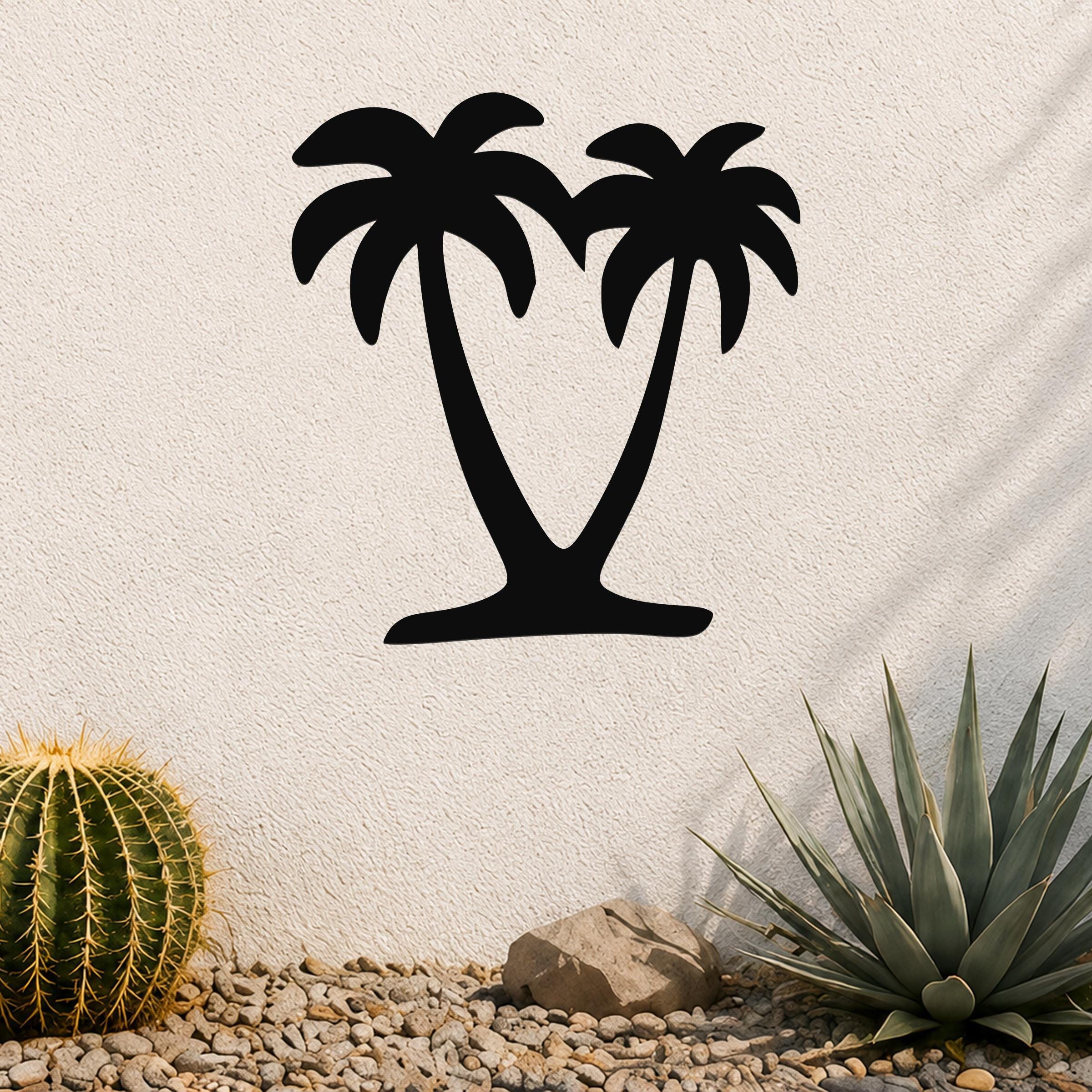 Black metal palm tree wall art with two silhouetted trunks and fronds, mounted on a textured outdoor wall above a gravel garden with cacti and succulents.