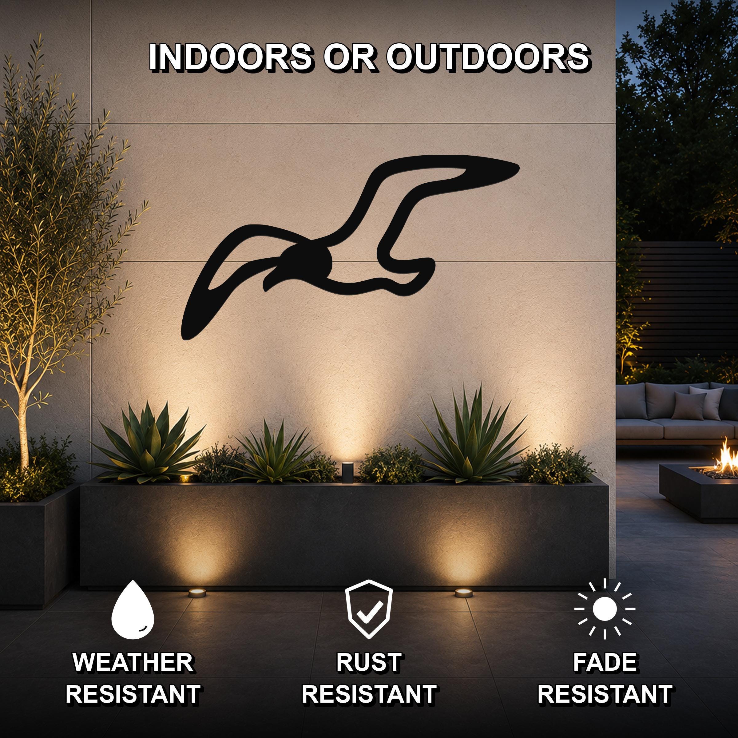 Black metal seagull wall art with motion-line cutouts, mounted on an outdoor wall above a planter in a patio setting.