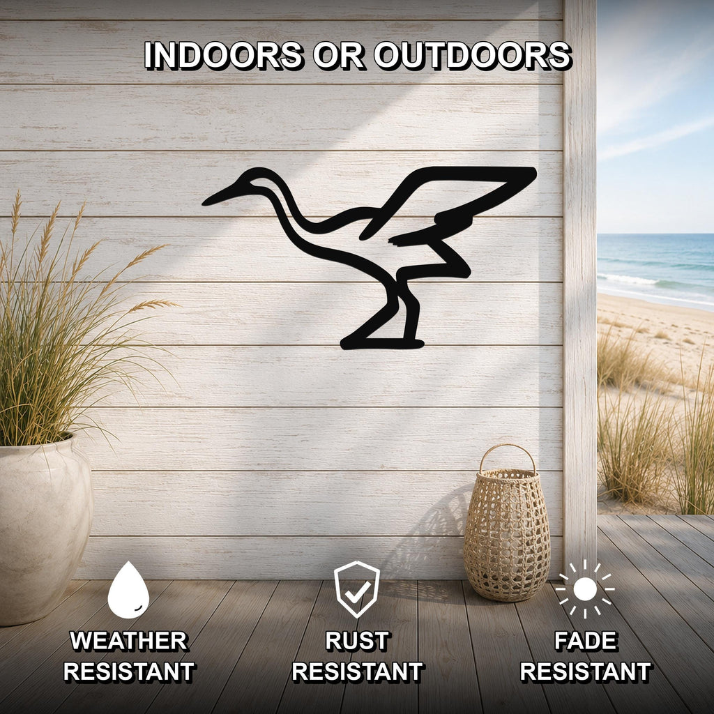 Black metal crane wall art silhouette mounted on a light wood plank wall, displayed on a patio with a beach view, weather resistant, rust resistant, and fade resistant.