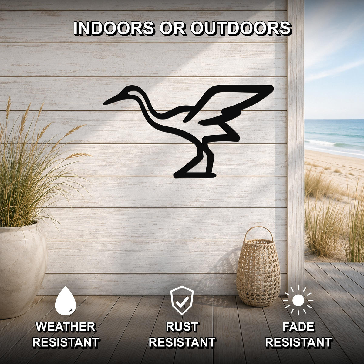Black metal crane wall art silhouette mounted on a light wood plank wall, displayed on a patio with a beach view, weather resistant, rust resistant, and fade resistant.